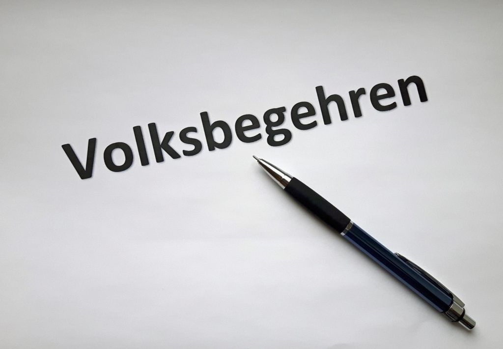 Das Wort 'Volksbegeehren' steht auf einem weißen Hintergrund mit einem Stift in der Nähe.