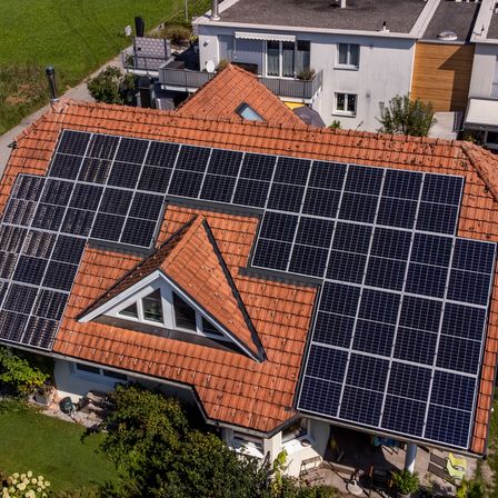 Luftaufnahme eines Hauses mit Solarmodulen auf dem Dach und einem kleinen Garten davor.