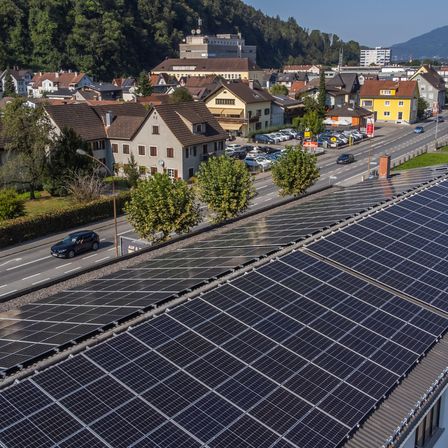 Luftaufnahme einer Stadt mit Solarmodulen auf einem Dach in der Nähe einer Straße mit Autos und einem Parkplatz.