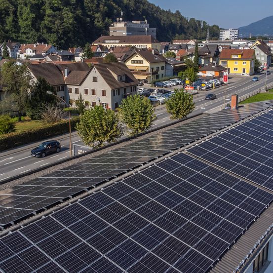 Luftaufnahme einer Stadt mit Solarmodulen auf einem Dach in der Nähe einer Straße mit Autos und einem Parkplatz.