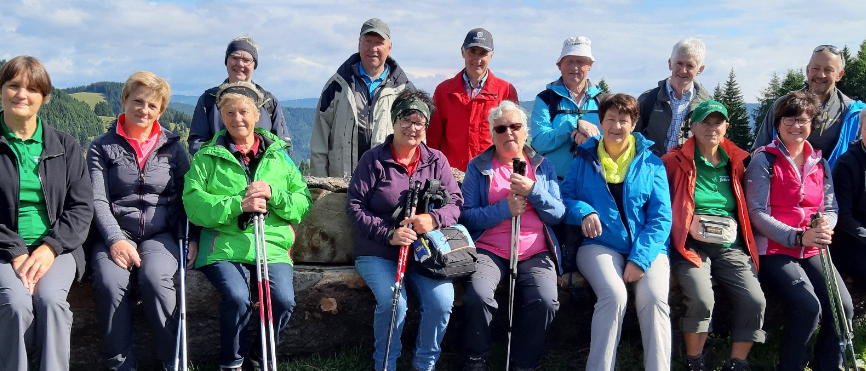 Eine Gruppe von Wanderern, alle in warme Kleidung gekleidet, posiert für ein Foto auf einem Grashügel mit Bergen im Hintergrund.
