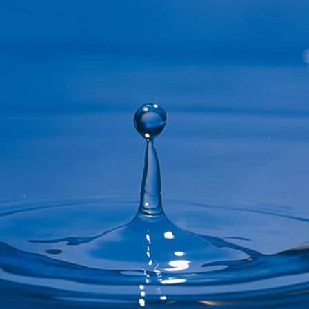 Ein Wassertropfen fällt in einen blauen Wasserkörper und erzeugt Wellen und Reflexionen.