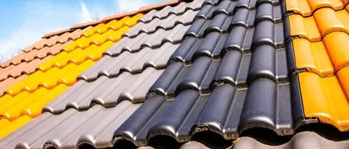 Ein Dach mit drei Abschnitten, jeder in einer anderen Farbe gestrichen: gelb, grau und schwarz. Der Himmel ist blau mit einigen Wolken.