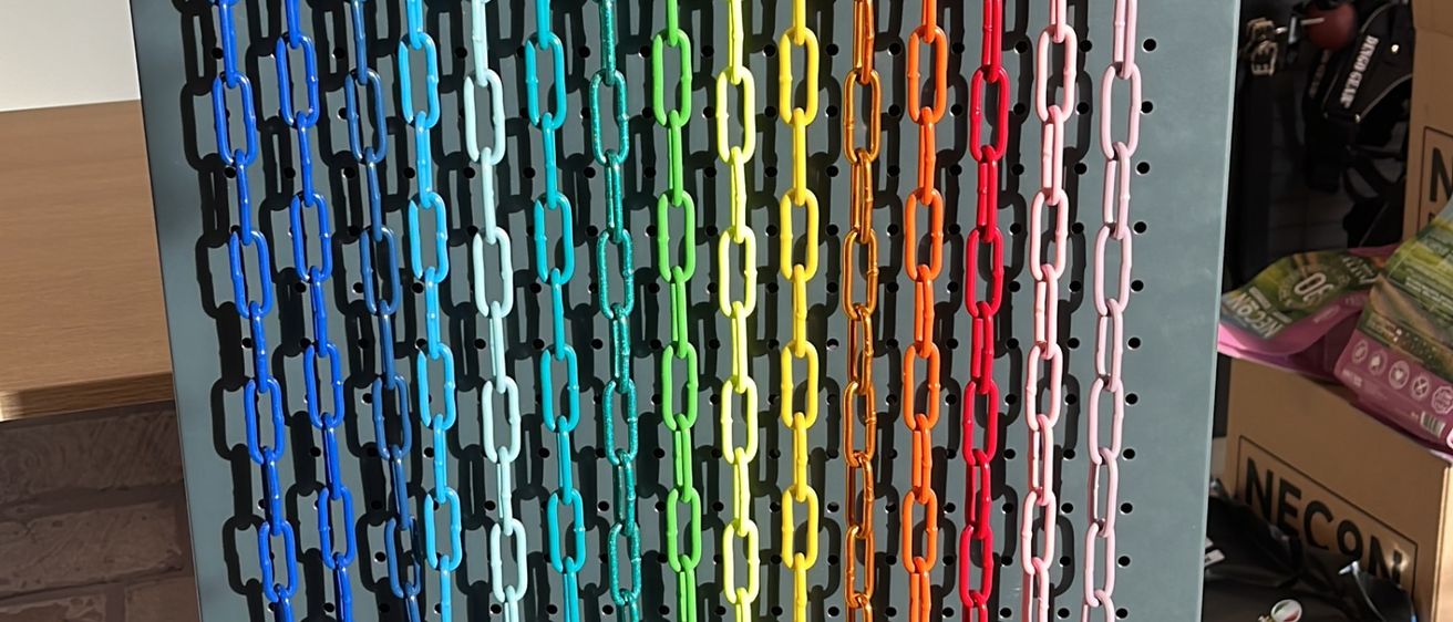 Eine Ausstellung von farbenfrohen Kettenleinen für Haustiere, aufgehängt an einer Metallwand mit Haken, neben verschiedenen Hundehalsbändern und Spielzeug.