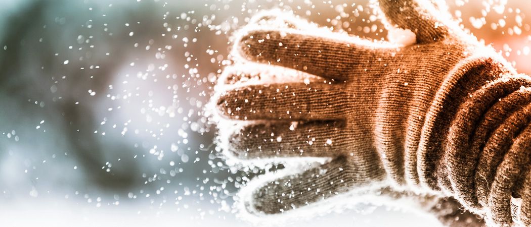 Eine behandschuhte Hand mit Schnee darauf, Schneeflocken fallen vor einem unscharfen Hintergrund.
