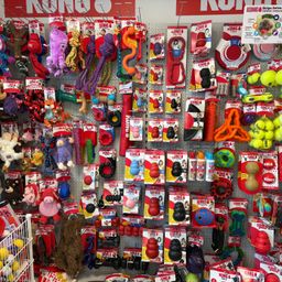 Eine Wand in einem Tierladen zeigt verschiedene KONG-Markenspielzeuge, darunter Bälle, Seile und Kauspielzeug. Die Wand ist mit farbenfrohen Verpackungen gefüllt, die verschiedene Produkte für Haustiere präsentieren.