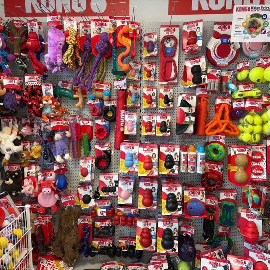 Eine Wand in einem Tierladen zeigt verschiedene KONG-Markenspielzeuge, darunter Bälle, Seile und Kauspielzeug. Die Wand ist mit farbenfrohen Verpackungen gefüllt, die verschiedene Produkte für Haustiere präsentieren.