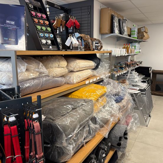 Ein Blick in den Innenbereich eines Geschäfts mit verschiedenen Artikeln auf Regalen. Einige Artikel sind in Plastik eingewickelt, und im Hintergrund befinden sich Kisten und Taschen.