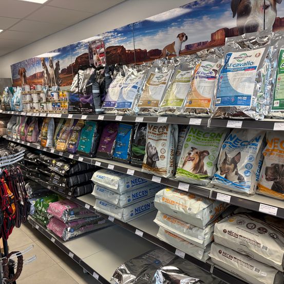 Ein Ladengang mit verschiedenen Tierfutterprodukten zur Schau. Säcke mit Hundefutter und anderen Haustierbedarfsartikeln sind auf Regalen angeordnet.