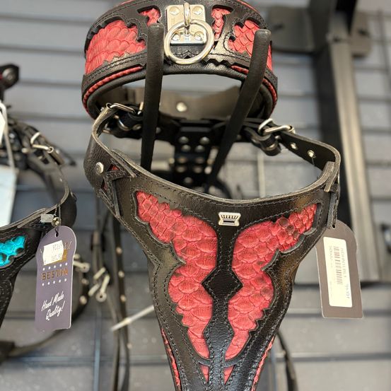 Ein schwarz-roter Lederhalsriemen mit Silberbeschlägen hängt an einem Ausstellungsständer und zeigt ein aufwendiges rotes Design.