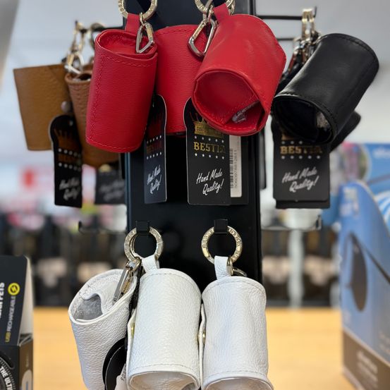 Eine Ausstellung von Leder-Golfhandschuhen in Rot, Schwarz und Weiß, die an einem Ständer hängen, mit 'Hand Made Quality!'-Etiketten.