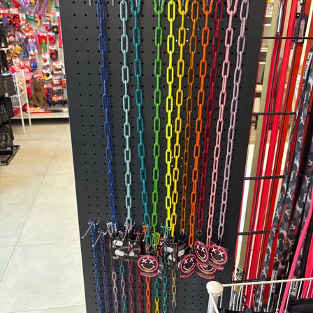 Eine farbenfrohe Ausstellung von Ketten mit Smiley-Gesicht-Tags hängt an einem schwarzen Lochbrett in einem Geschäft.