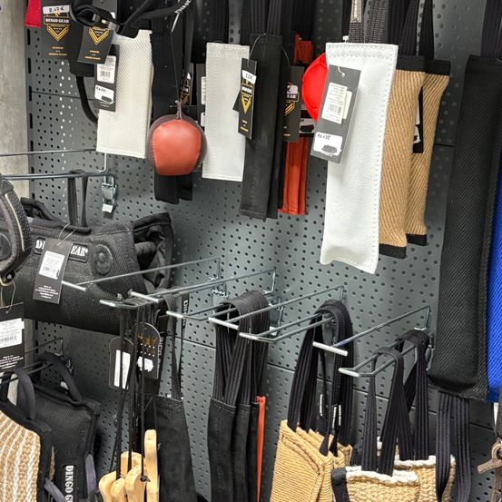 Ein wandmontiertes Display zeigt verschiedene Fitness-Zubehörteile, darunter schwarze und beige Taschen, rote und weiße Polsterung sowie einen roten Medizinball.