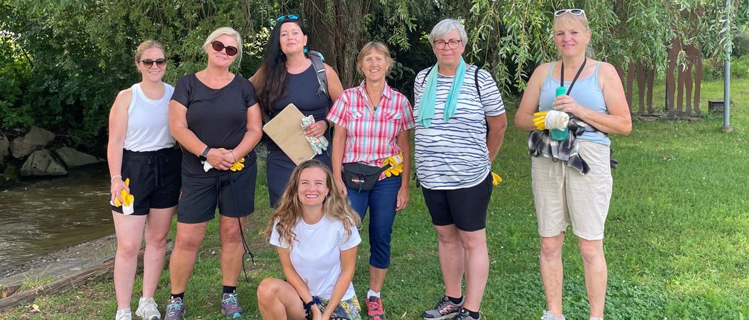 Eine Gruppe von Frauen in lässiger Kleidung steht und kniet auf einer Rasenfläche, möglicherweise für eine Gemeinschaftsveranstaltung. Sie lächeln und scheinen für ein Foto zu posieren.