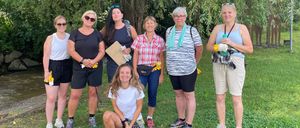 Eine Gruppe von Frauen in lässiger Kleidung steht und kniet auf einer Rasenfläche, möglicherweise für eine Gemeinschaftsveranstaltung. Sie lächeln und scheinen für ein Foto zu posieren.