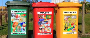 Drei Mülleimer stehen in einer Reihe. Ein grüner Behälter mit der Aufschrift Kompost, ein roter Behälter mit der Aufschrift Abfall und ein orangefarbener Behälter mit der Aufschrift Recyceln.
