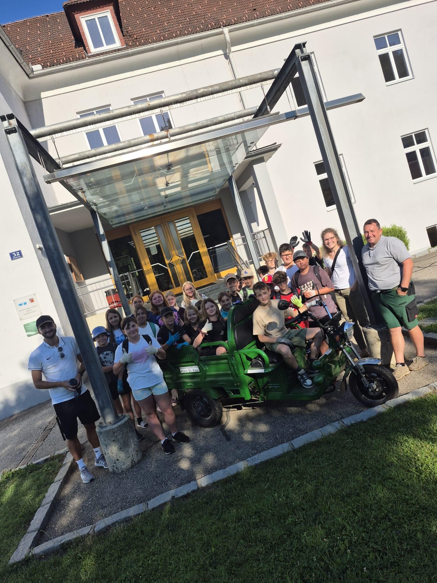 Eine Gruppe von Menschen posiert für ein Foto vor einem Gebäude mit einem grünen Fahrzeug davor.