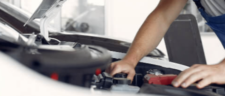 Ein Mann arbeitet an einem Automotor, trägt eine Schürze und Ärmel. Er scheint sich darauf zu konzentrieren, etwas im Motorraum zu reparieren.