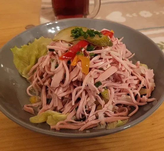 Eine Schüssel mit rosa Fleischsalat mit roten und gelben Paprikaschoten, Gurken und Frühlingszwiebeln auf einem Holztisch.