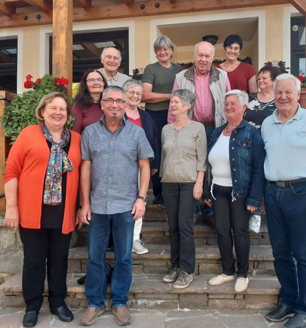 Eine Gruppe Erwachsener steht auf Steinstufen und lächelt für ein Gruppenfoto. Einige tragen Brillen und Schals.