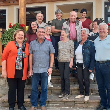 Eine Gruppe Erwachsener steht auf Steinstufen und lächelt für ein Gruppenfoto. Einige tragen Brillen und Schals.