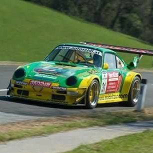 Ein leuchtend grünes und gelbes Rennauto rast eine kurvenreiche Strecke hinunter. Das Auto hat die Nummer 30 auf der Seite und Sponsorenlogos. Grünes Gras und Bäume säumen den Hintergrund.