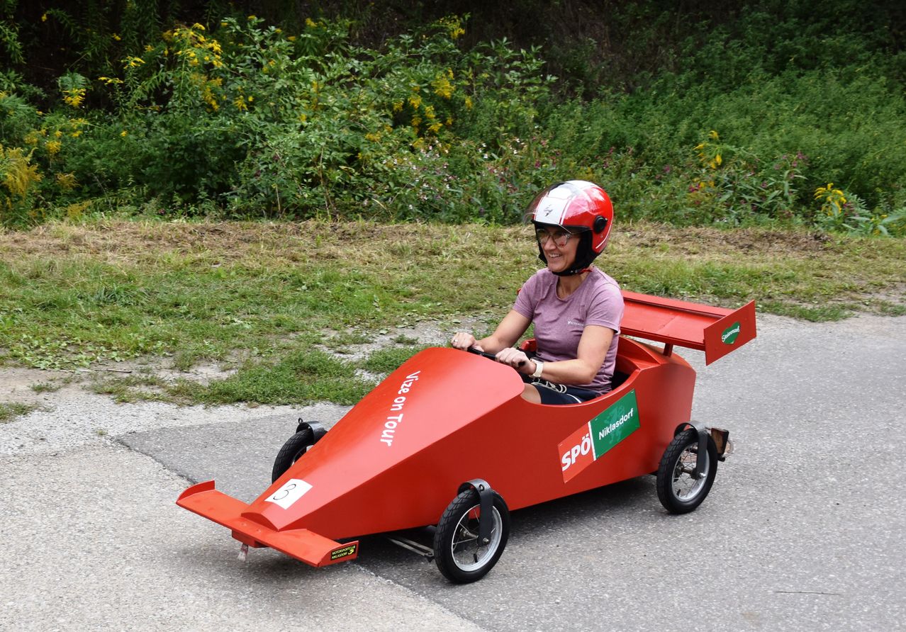 Eine Frau in einem roten Helm fährt einen roten Go-Kart auf einer Straße, mit 'SPO' und 'Nikolasdorf' auf der Seite.