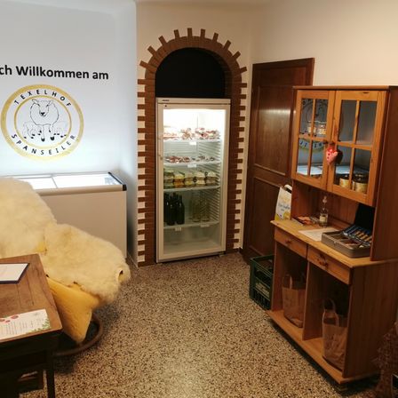 Ein Raum mit einem Willkommensschild an der Wand, einem Kühlschrank voller Lebensmittel, einem Holzschrank mit Glastüren und einem gemütlichen Stuhl.