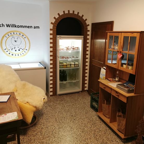 Ein Raum mit einem Willkommensschild an der Wand, einem Kühlschrank voller Lebensmittel, einem Holzschrank mit Glastüren und einem gemütlichen Stuhl.