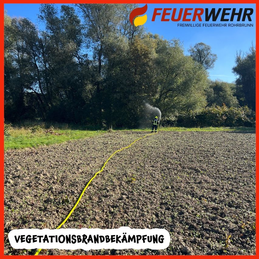 Ein Feuerwehrmann sprüht Wasser aus einem Schlauch auf einem Feld. Das Feld ist trocken und mit kleinen Pflanzen bedeckt. Im Hintergrund stehen Bäume. Die Worte 'Vegetationsbrandbekampfung' sind in weiß geschrieben.