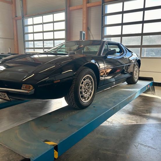 Ein schwarzer Sportwagen steht auf einem Heber in einer Garage. Er hat ein Nummernschild mit der Aufschrift '47-DF'. Das Auto ist angehoben und wird von einer blauen Plattform gestützt.