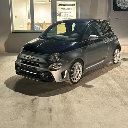 Ein schwarzer Fiat 500 Sportwagen mit silbernen Felgen und einem silbernen Streifen, geparkt in einer Garage.
