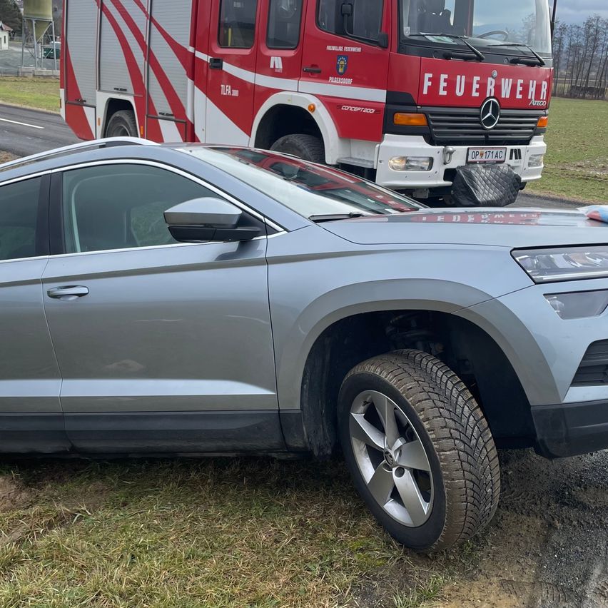Ein silberner SUV ist am Straßenrand geparkt, mit einem roten Feuerwehrfahrzeug dahinter. Der SUV hat sein Vorderrad auf dem Gras, und das Feuerwehrfahrzeug hat einen Gepäckkoffer auf dem Rücken.