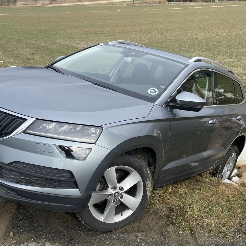 Ein grauer SUV mit einem platten Reifen steht am Straßenrand, in einem Grasfeld.