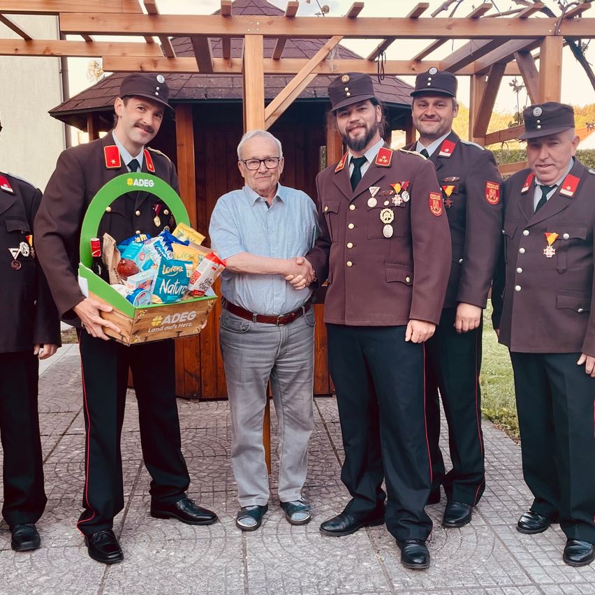 Eine Gruppe von Männern in Uniform, darunter ein Mann mit einem Schnurrbart, erhalten einen Korb mit Snacks von einem Mann in einem blauen Hemd.