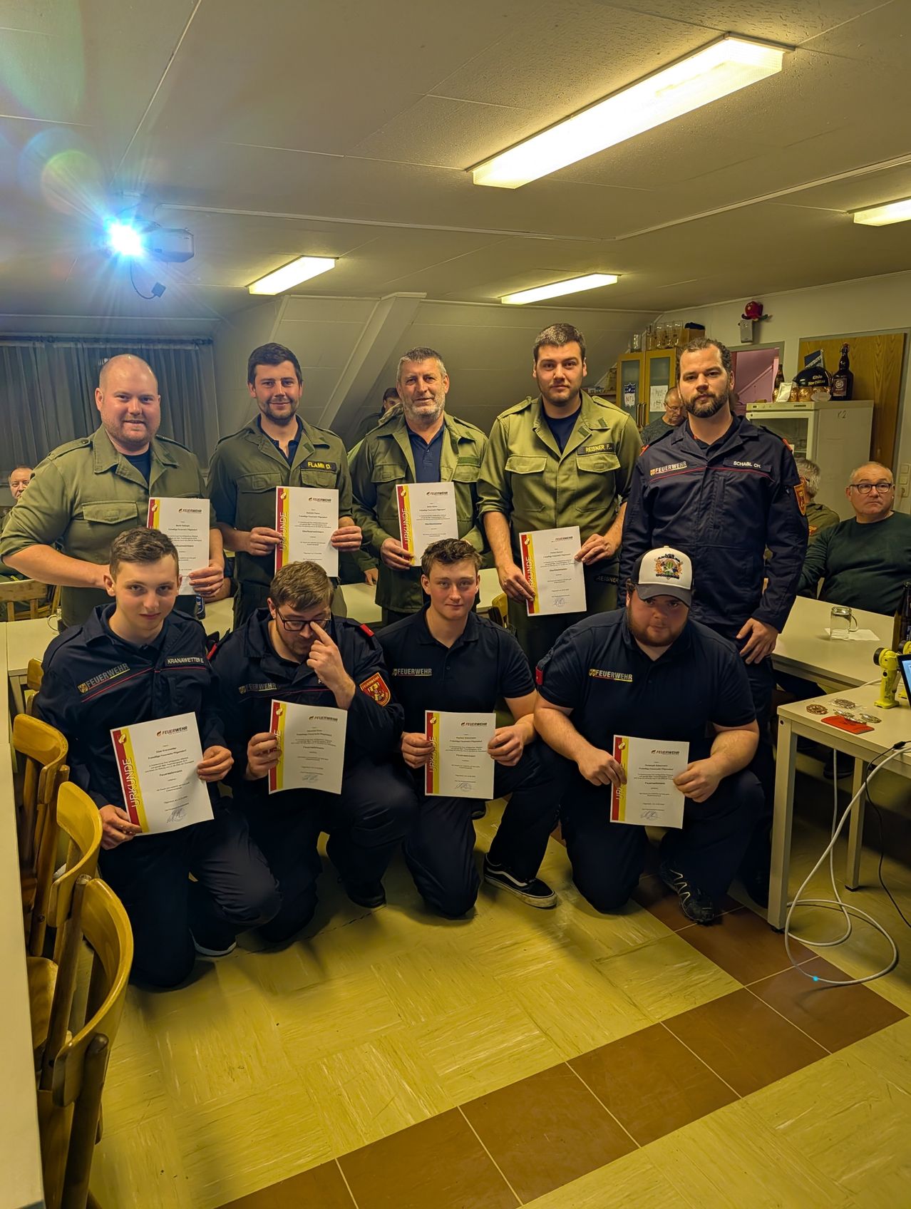 A group of firefighters in uniform hold certificates and pose for a photo in a room.