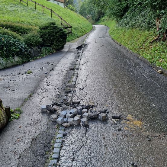 Eine beschädigte Straße mit einem Haufen Steine und Trümmerteilen auf der Seite, zusammen mit einem grün bewachsenen Hügel und einem Zaun.