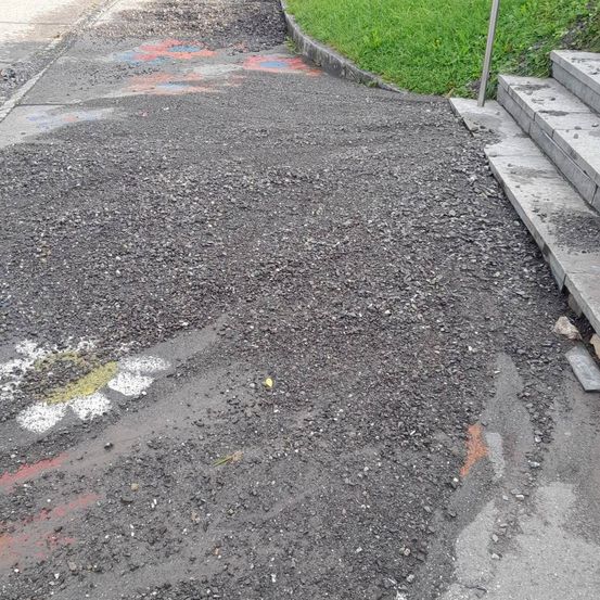 Eine Nahaufnahme einer mit kleinen Steinen bedeckten Straße, mit einer weißen und gelben blumenartigen Markierung und etwas roter Farbe.