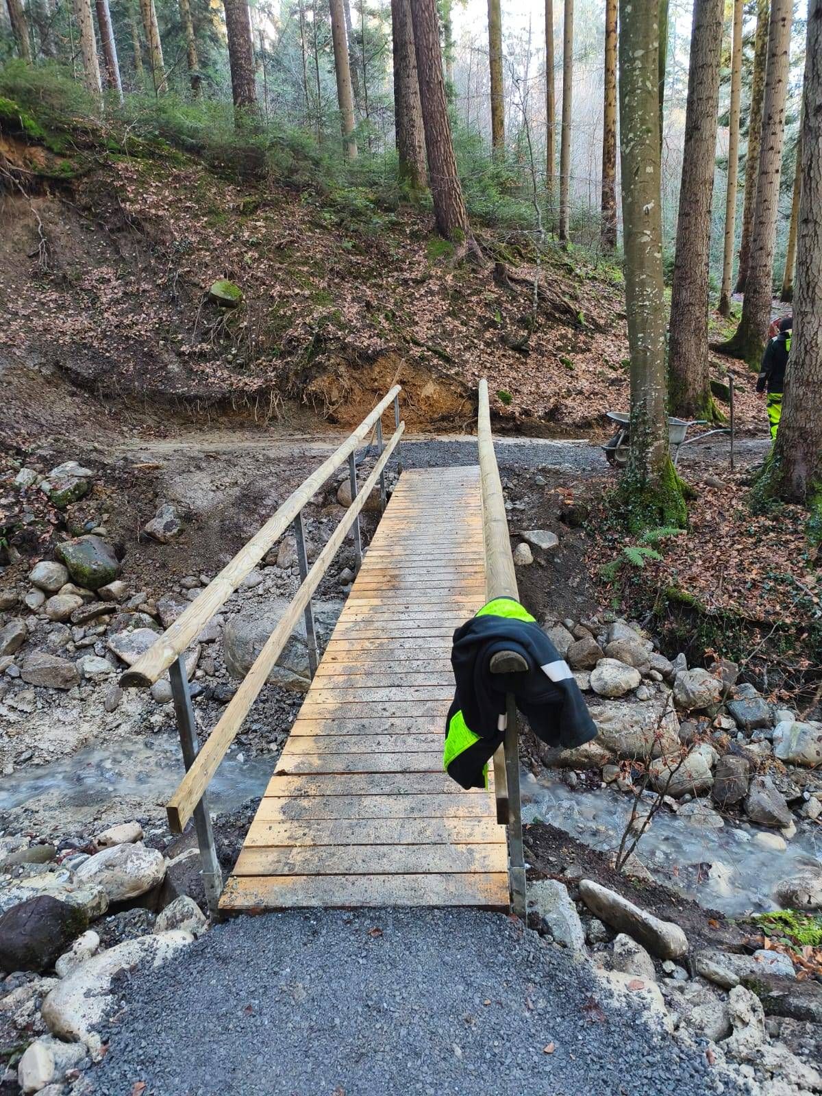 Eine Holzbrücke im Bau in einem Wald mit einer Jacke, die an den Geländern hängt.