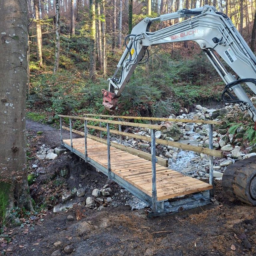 Eine Holzbrücke im Bau in einem Wald, in der Nähe eines weißen Baggers.