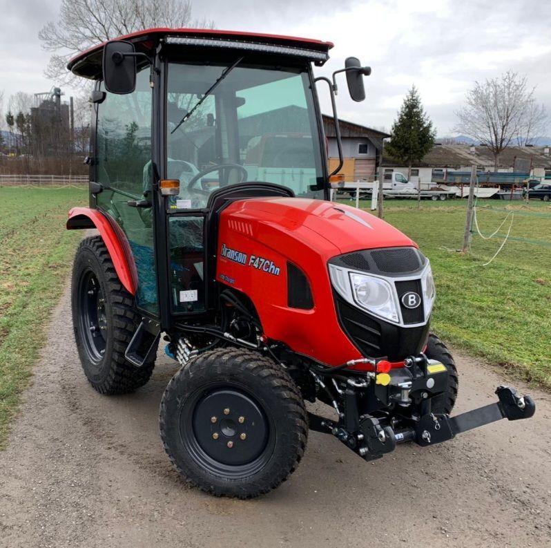 Ein roter Branson F47Ch Traktor steht auf einem Feldweg, mit einem Grasfeld und Bäumen im Hintergrund.