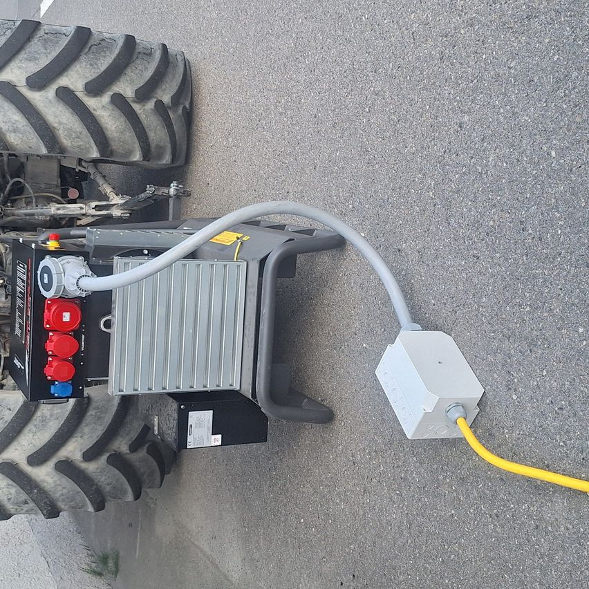 Die Rückseite eines Traktors mit einer angeschlossenen Stromsteckdose und einem gelben Kabel. Der Traktor hat einen großen Reifen und eine Metallbox mit roten und blauen Steckern.