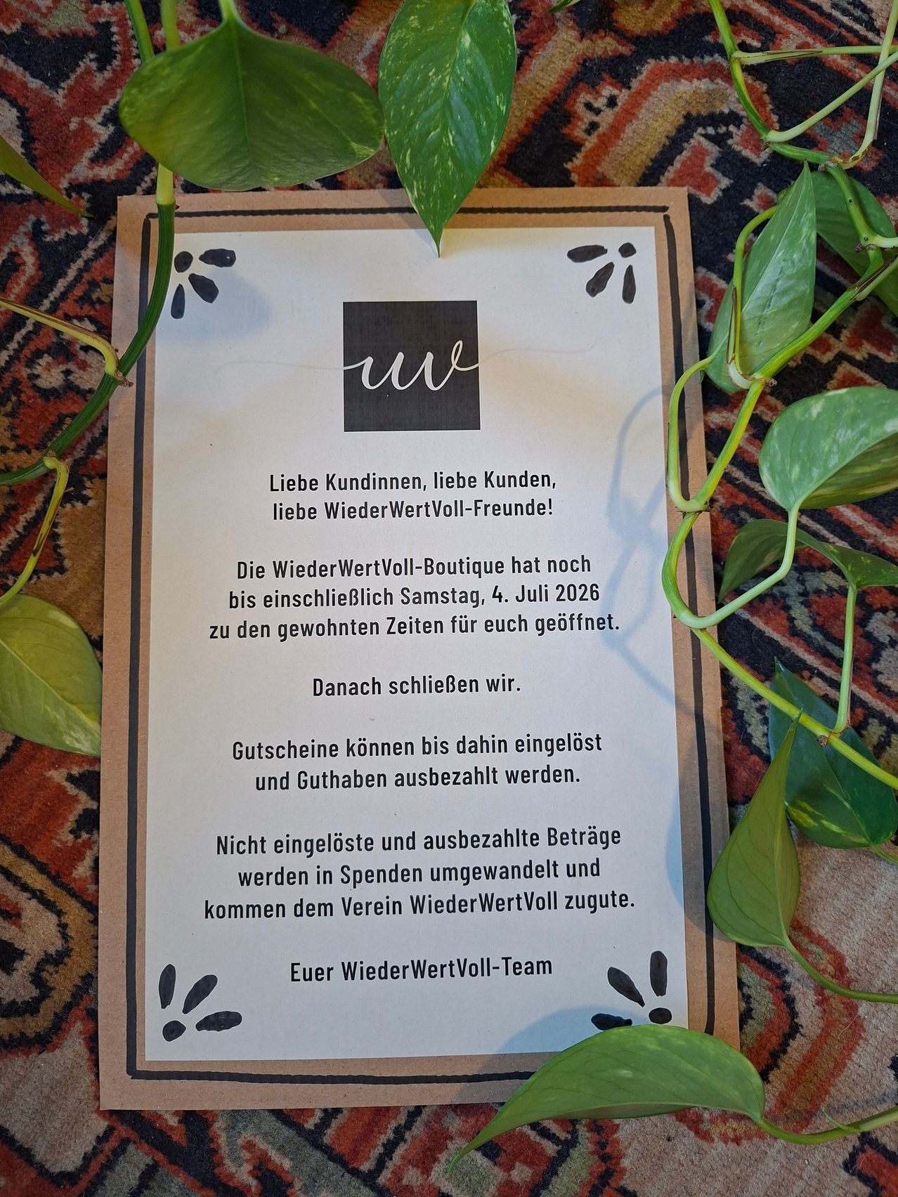 A sign on a carpeted surface announces the closing of WiederWertVoll boutique. It invites customers to shop until July 4, 2026. It also mentions that vouchers can be redeemed and accounts settled up to that date. Unredeemed and unsettled items will be donated to WiederWertVoll.