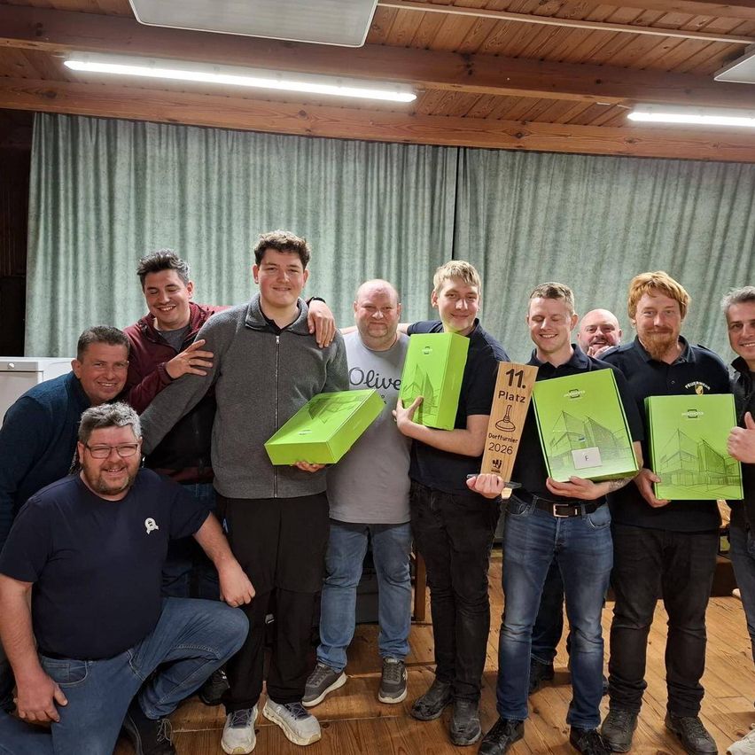 Eine Gruppe von Männern posiert für ein Foto, während sie grüne Schachteln und einen Pokal halten. Sie befinden sich in einem Raum mit Holzboden und einer Gardine.