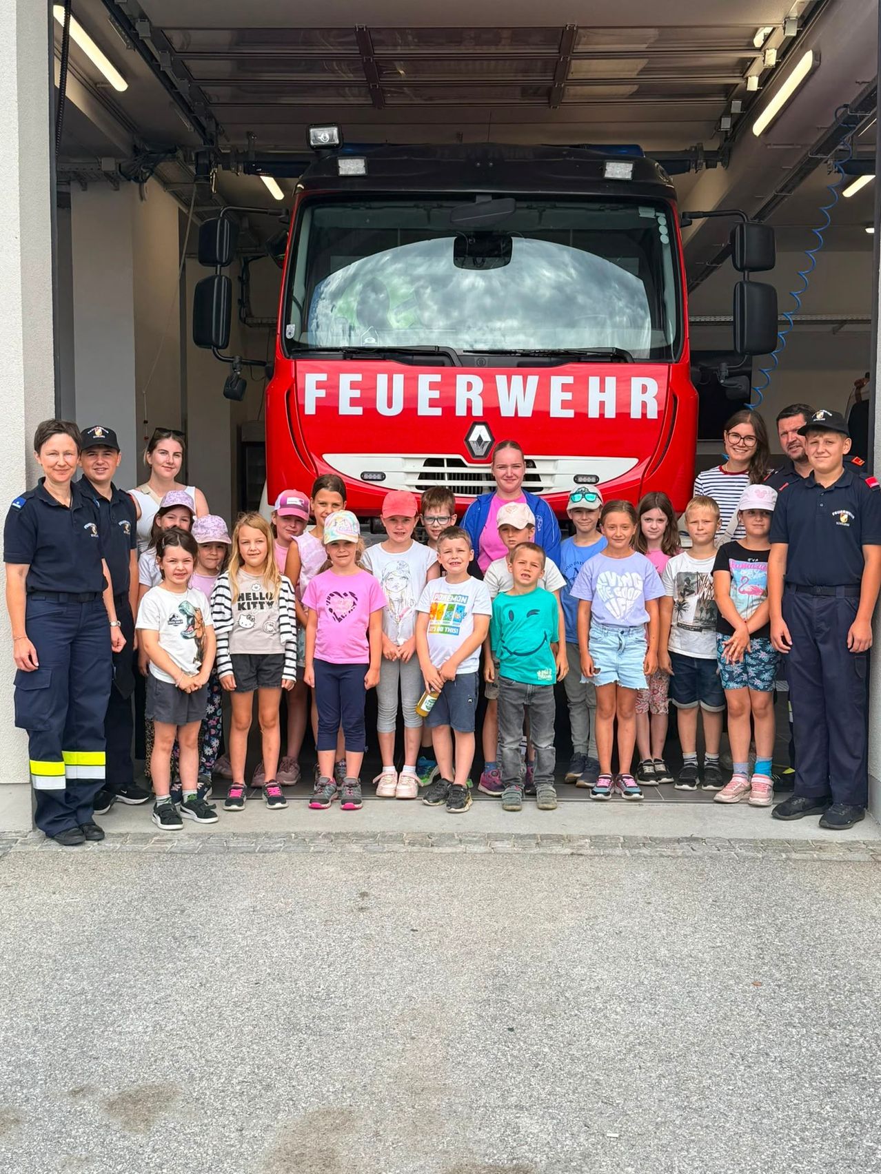 Eine Gruppe von Kindern und Erwachsenen posiert für ein Foto vor einem roten Feuerwehrauto. Das Feuerwehrauto steht in einer Garage.