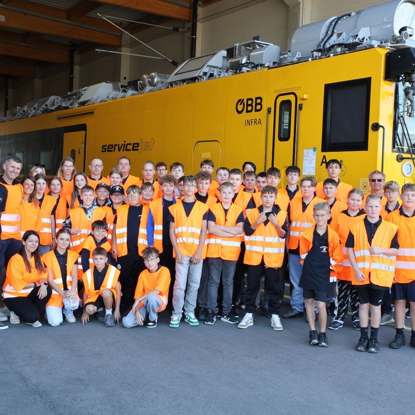 Eine Gruppe von Menschen in orangefarbenen Westen posiert für ein Foto vor einem gelben Zug.