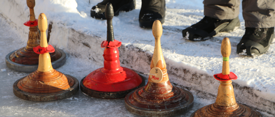 Drei farbige Curling-Steine sind auf einer verschneiten Oberfläche platziert. Ein schwarzer Stiefel ist teilweise mit Schnee bedeckt.