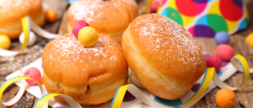 Drei pulverisierte Donuts auf einem Holztisch. Sie sind mit bunten Süßigkeiten und Bändern dekoriert. Der Hintergrund ist unscharf.