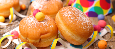 Drei pulverisierte Donuts auf einem Holztisch. Sie sind mit bunten Süßigkeiten und Bändern dekoriert. Der Hintergrund ist unscharf.