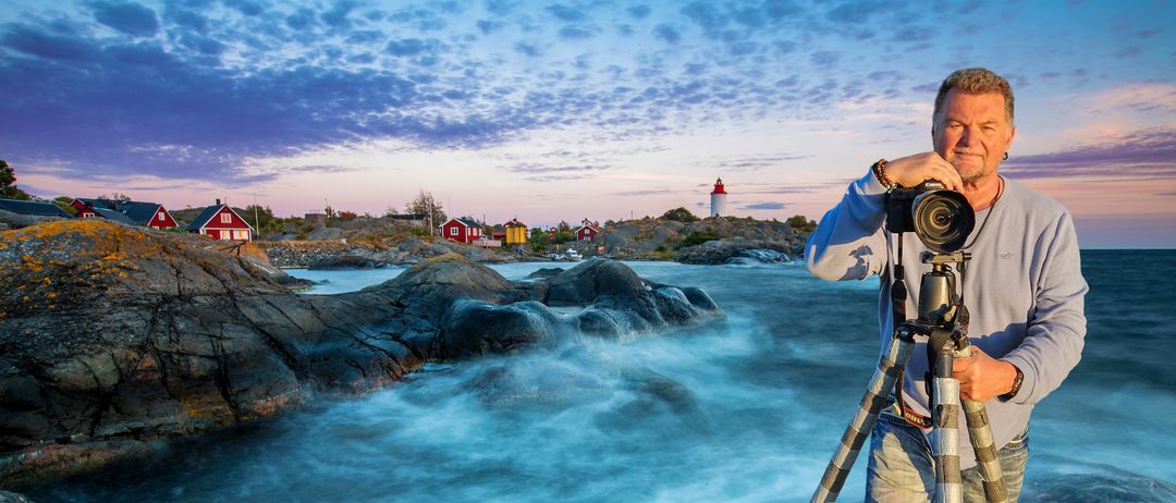 Eine ruhige Küstenlandschaft mit einem Leuchtturm auf einem felsigen Hügel, umgeben von kleinen bunten Häusern. Das Meer ist ruhig mit sanften Wellen.